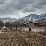 Kashmir Valley winter landscape with dry fields and distant mountains, apple orchards and saffron fields under cloudy skies, rural agriculture setting, climate stress visual, realistic documentary photography, natural colors, no text, no logos